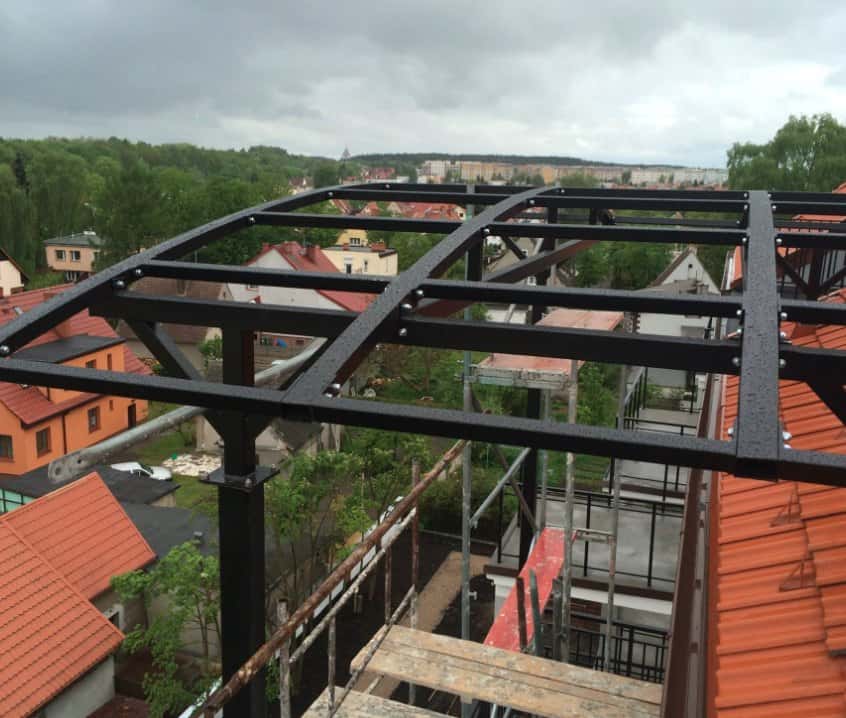 Skręcana stalowa rama zadaszenia na dachu, w tle dachy i osiedle